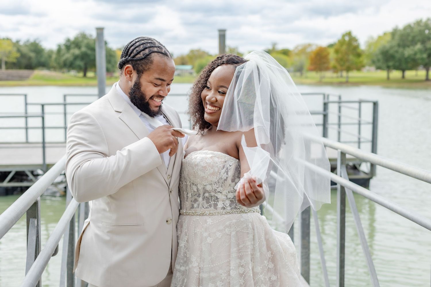 Newlyweds sharing tender moment on wooden dock by lake.