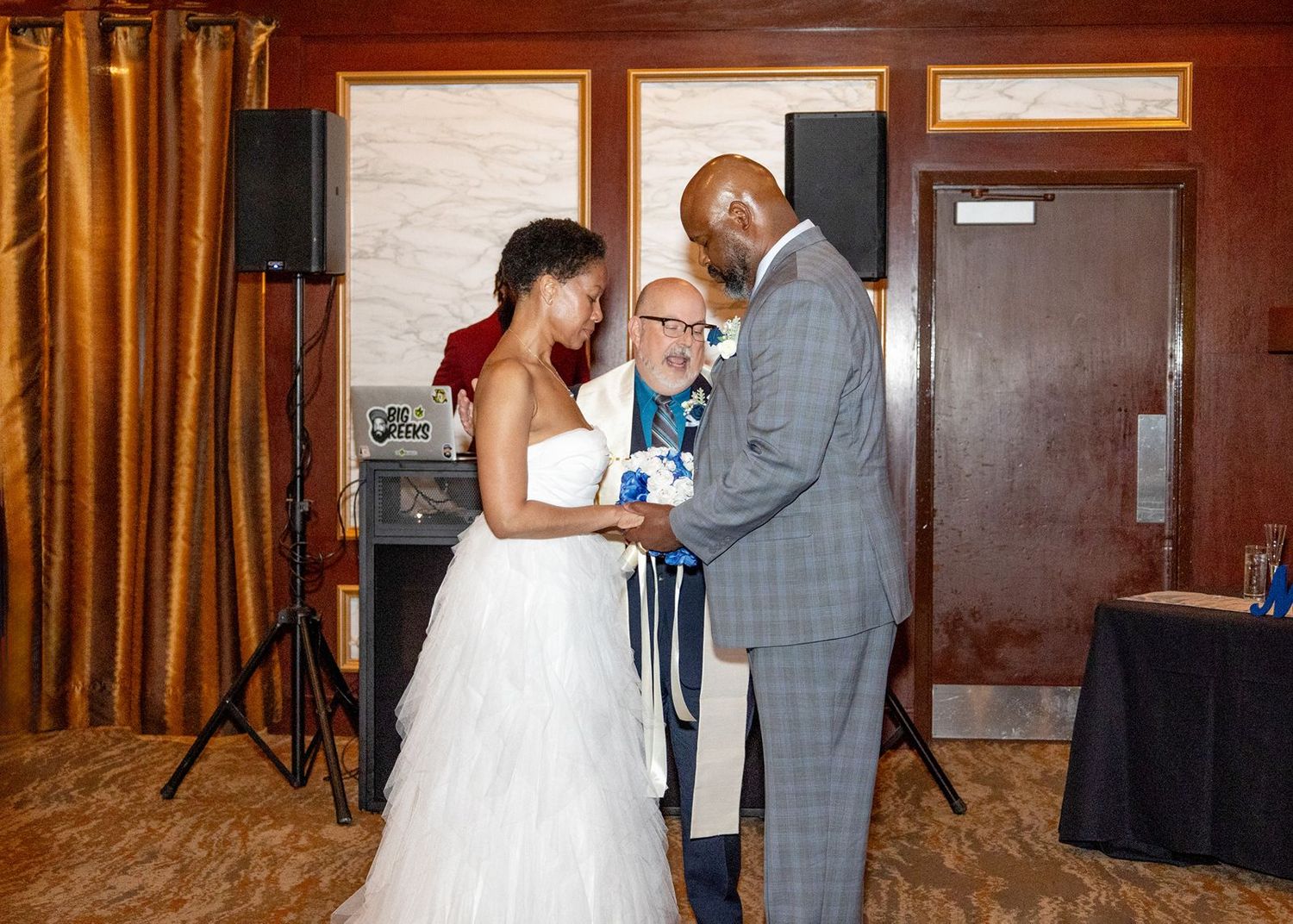 Bride and groom exchange vows with officiant during indoor wedding ceremony in elegant venue.