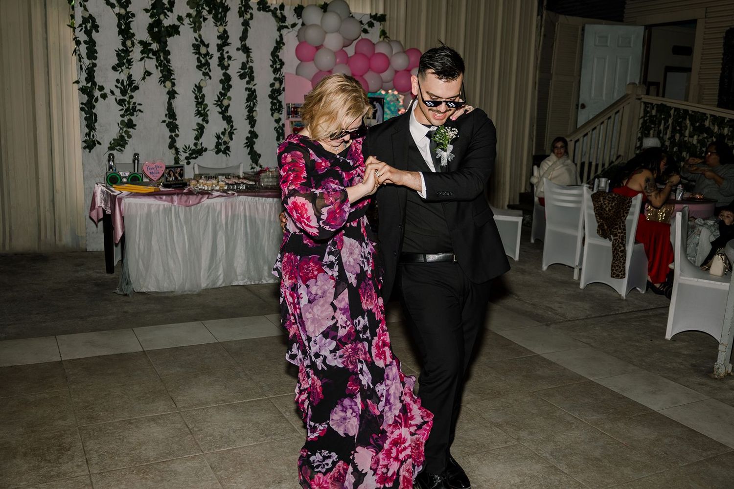 Elderly woman in floral dress dancing with man in suit at elegant wedding reception venue.