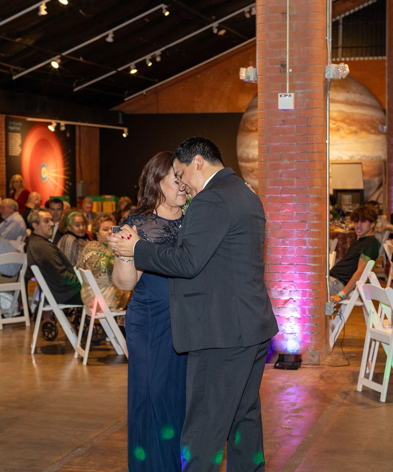 Couple shares intimate slow dance at wedding reception with seated guests watching.