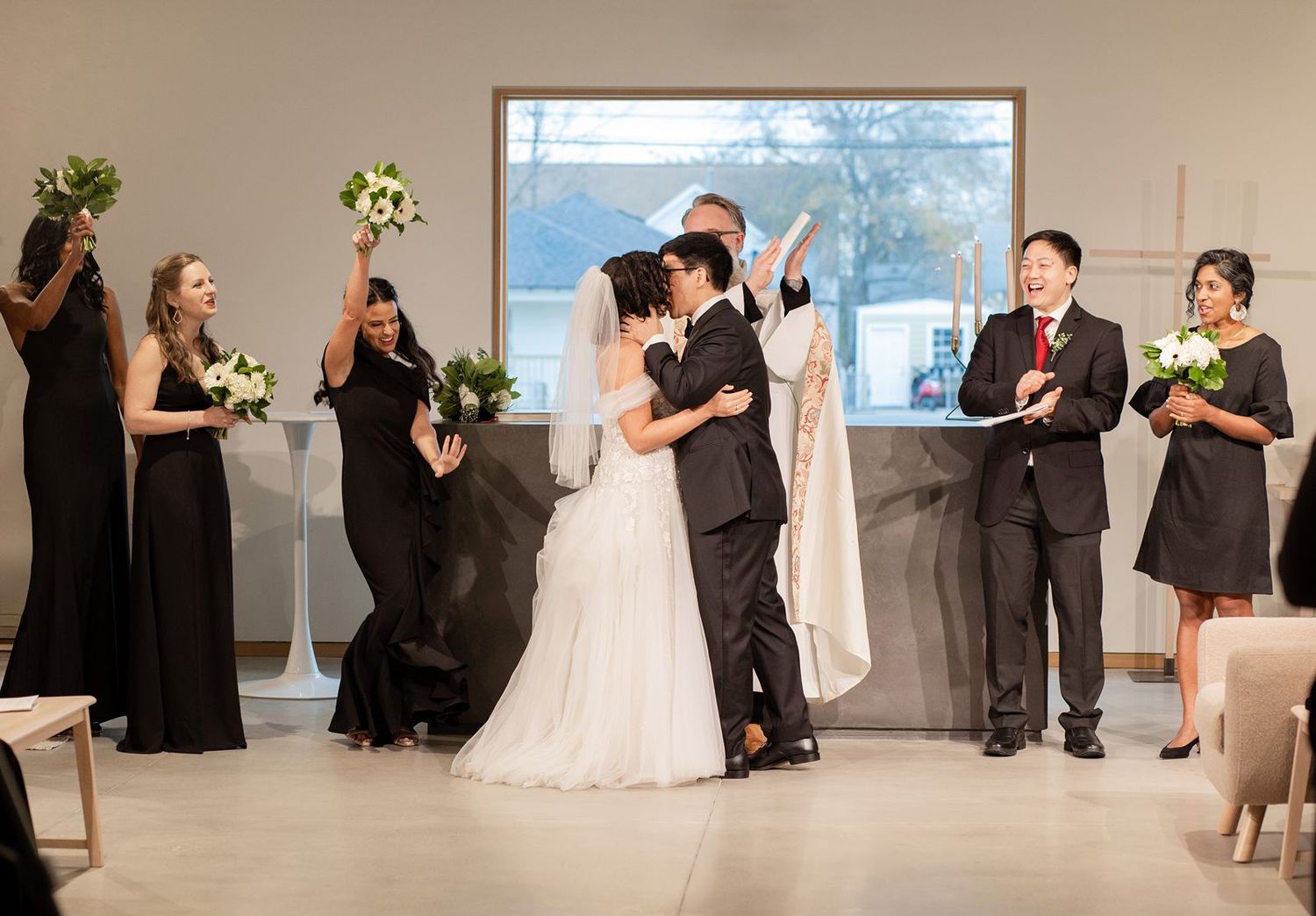 A panoramic view of a wedding ceremony with attendees in formal black and white attire in a bright indoor space.