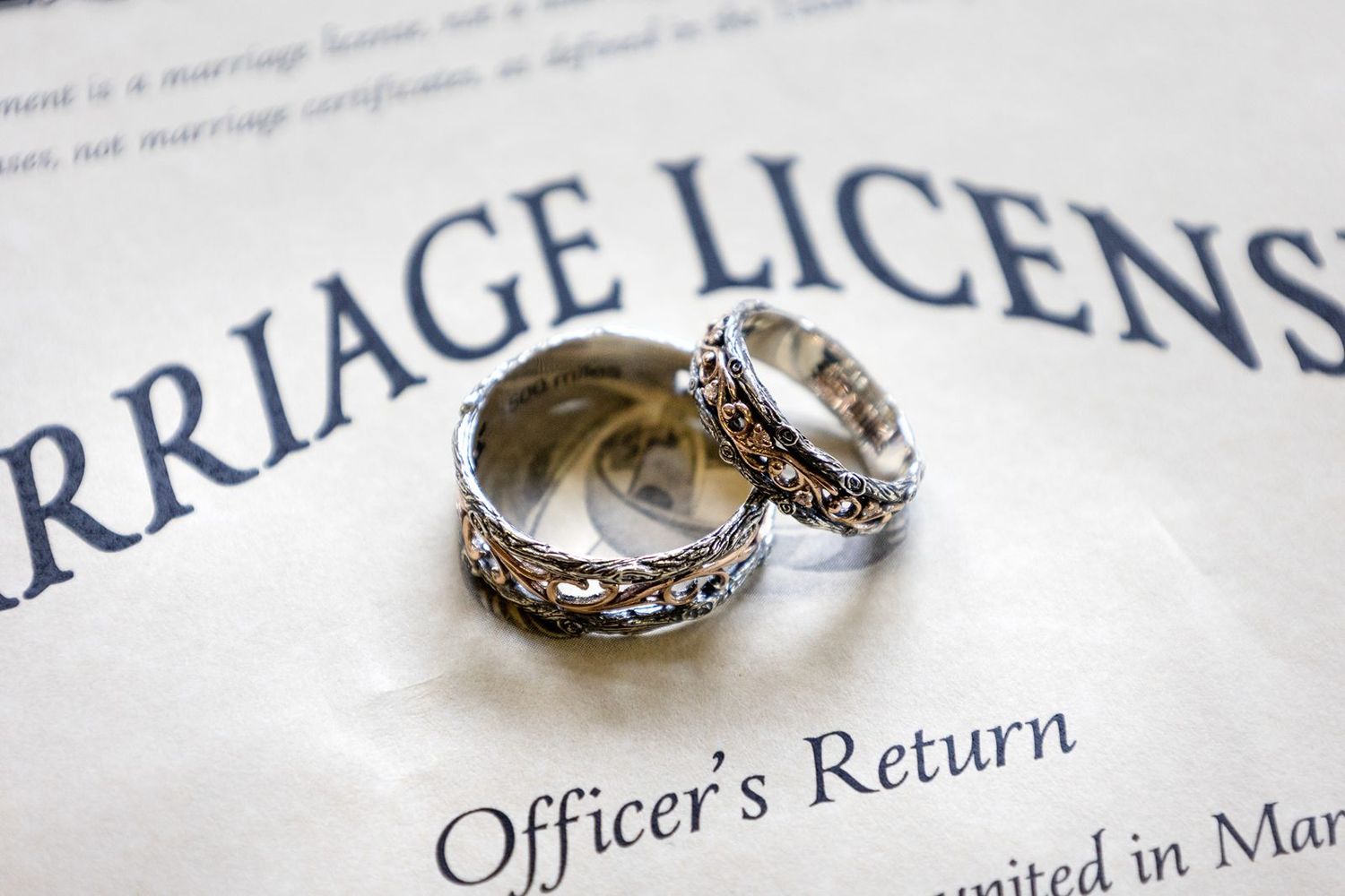 Two ornate silver and gold wedding bands resting on a marriage license document.
