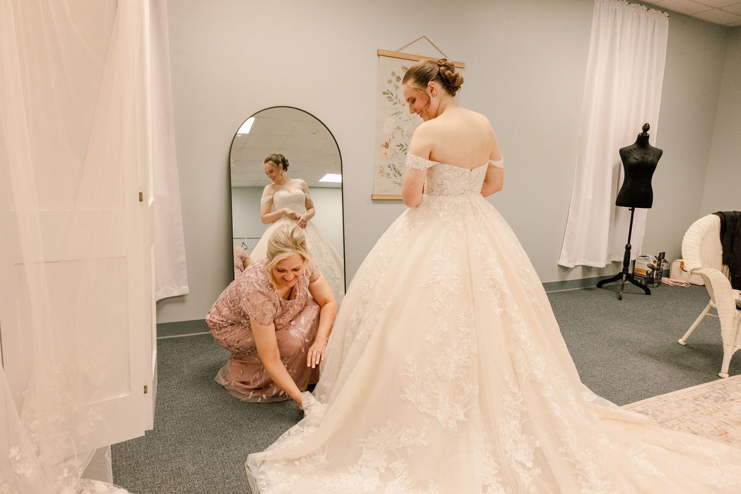 Bridesmaids assist with wedding dress preparations in cream colored dressing room.
