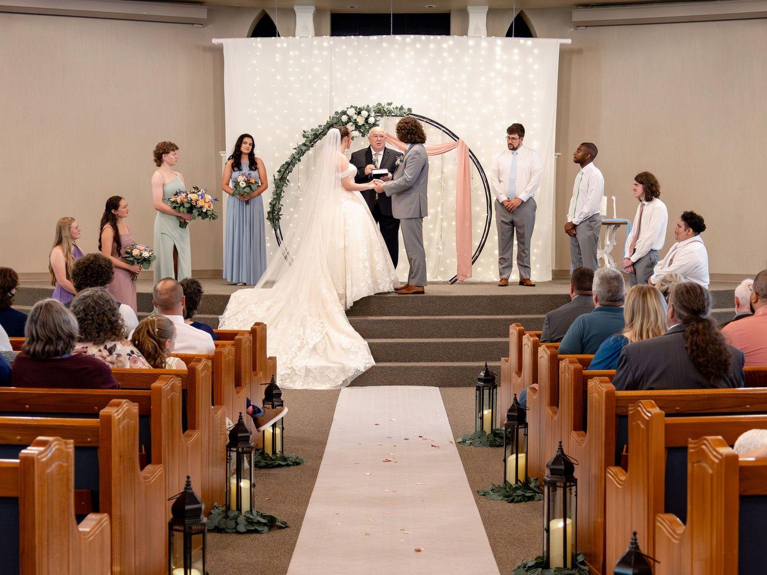 Wedding ceremony takes place under an archway with twinkle light backdrop in church.