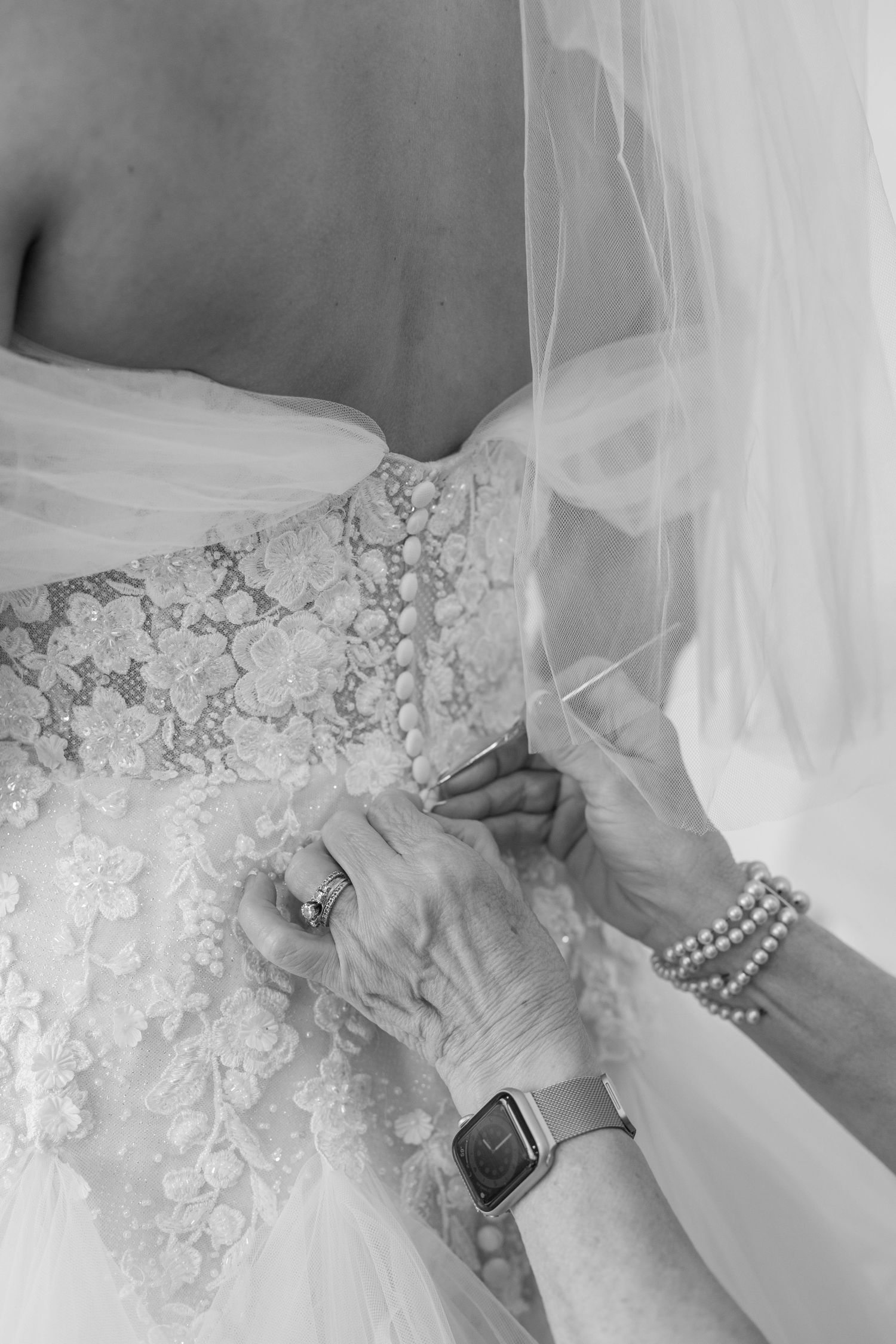 Close-up of hands adjusting delicate lace and beading details on an elegant white wedding dress.
