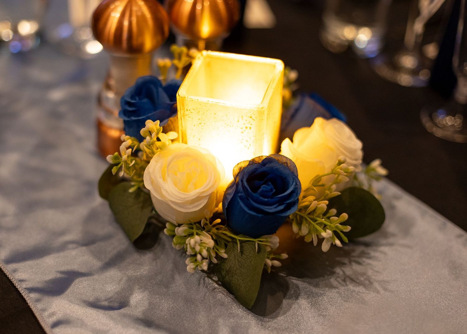 Wedding centerpiece with glowing candle and blue and white roses.