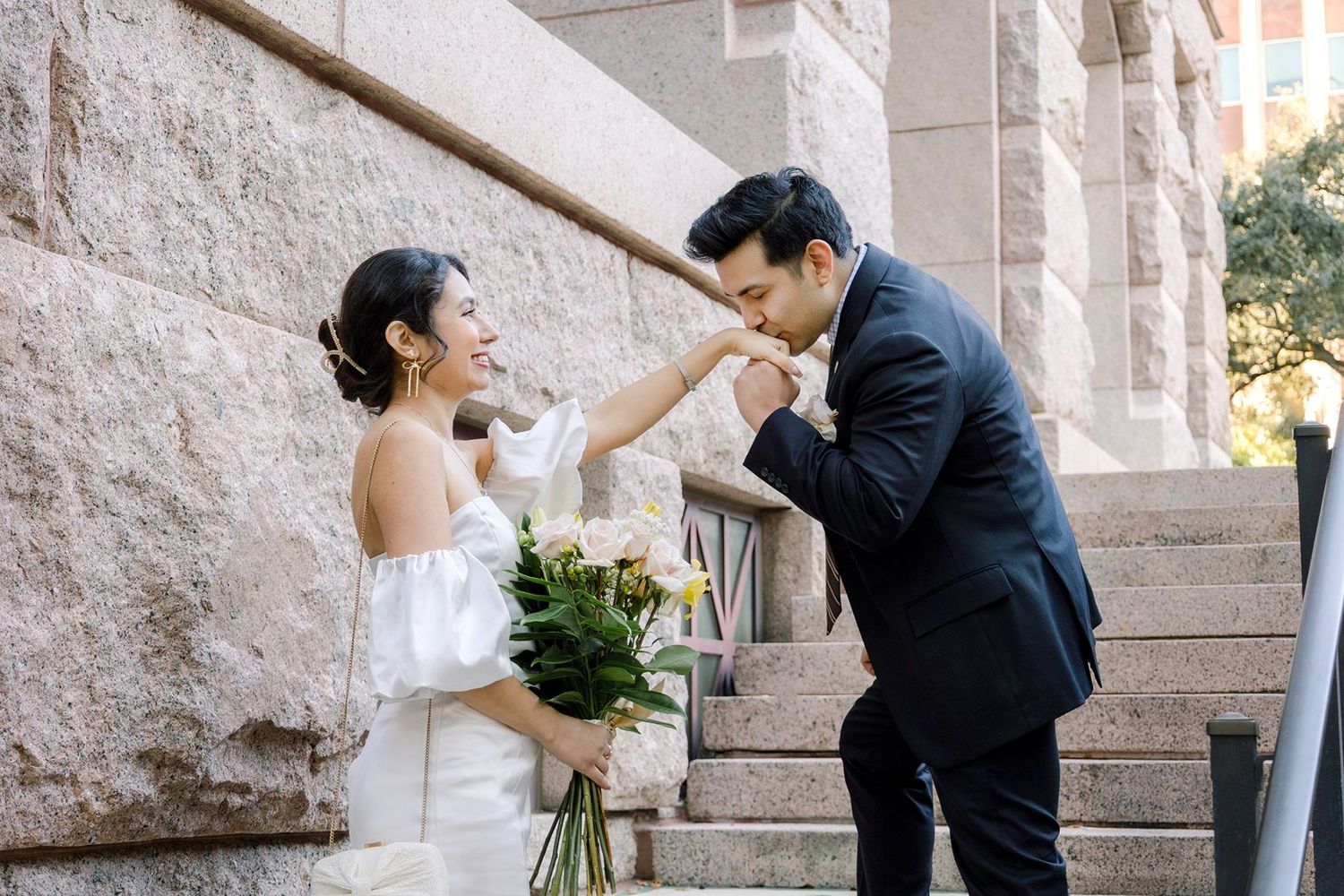 A couple shares romantic moments in front of a stone wall during their wedding photoshoot.