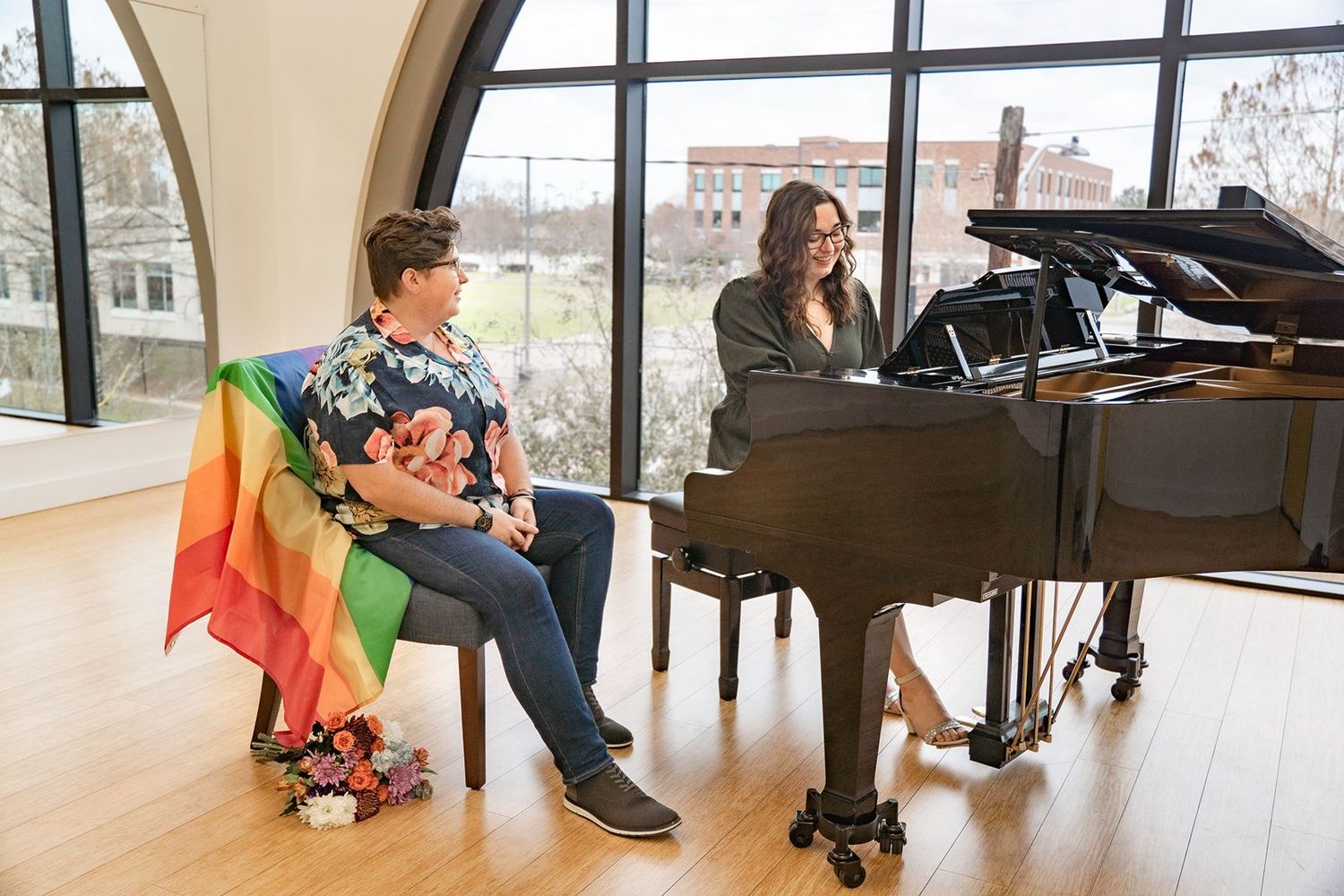 Students practicing at grand pianos in a bright modern music studio with large windows.