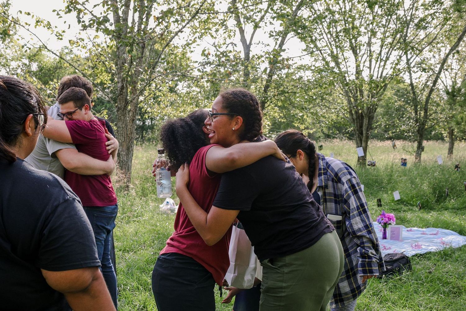 People hugging outdoors in a green park setting during an emotional gathering on a cloudy day.