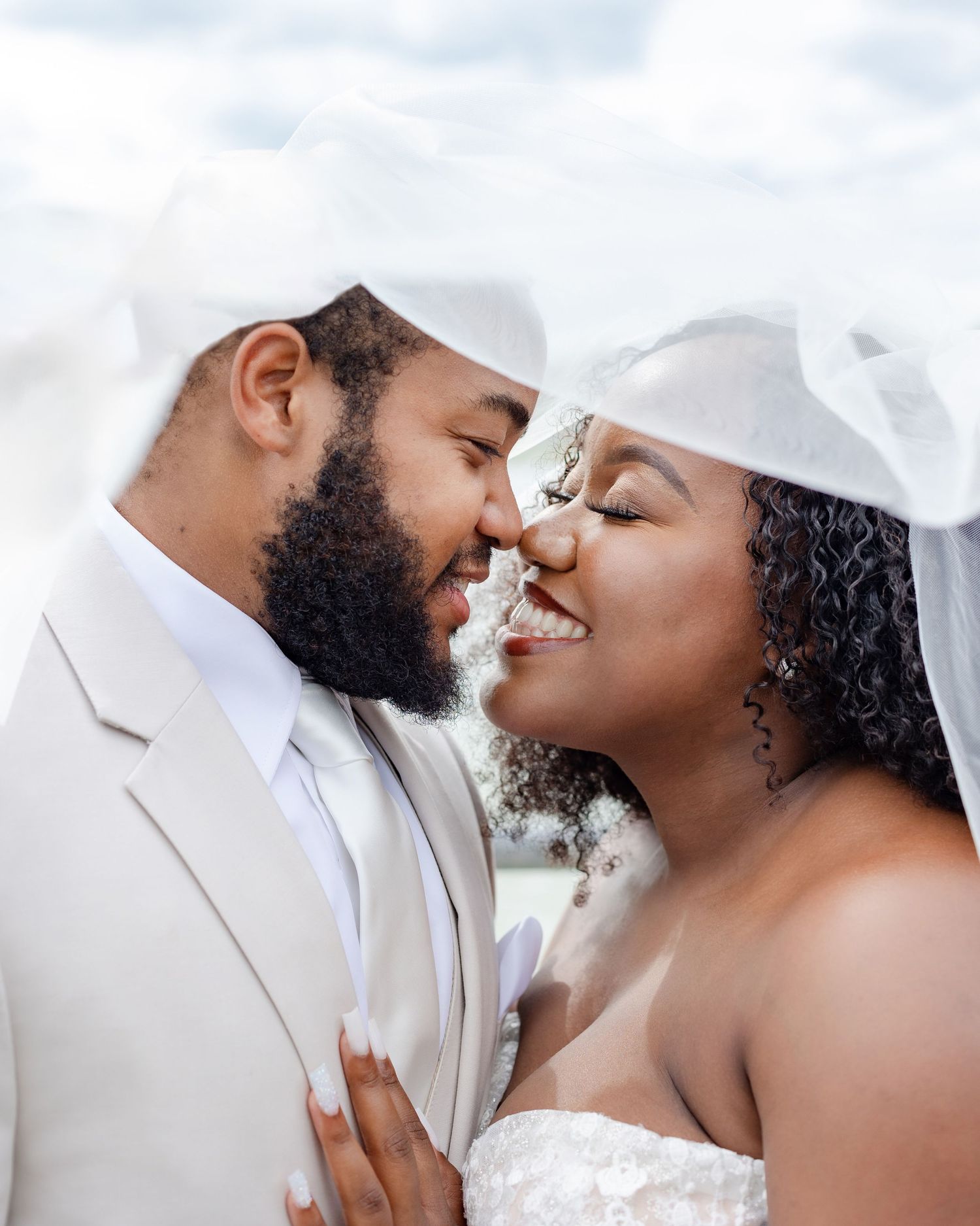 An intimate close-up portrait of newlyweds sharing a tender moment against a cloudy sky.