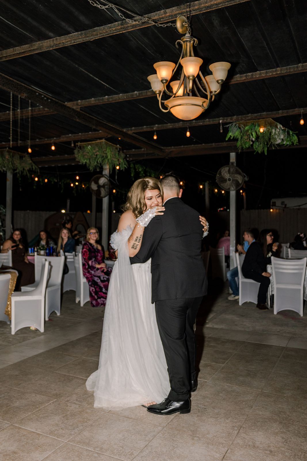Bride and groom share their first dance under a chandelier at an outdoor evening wedding reception.
