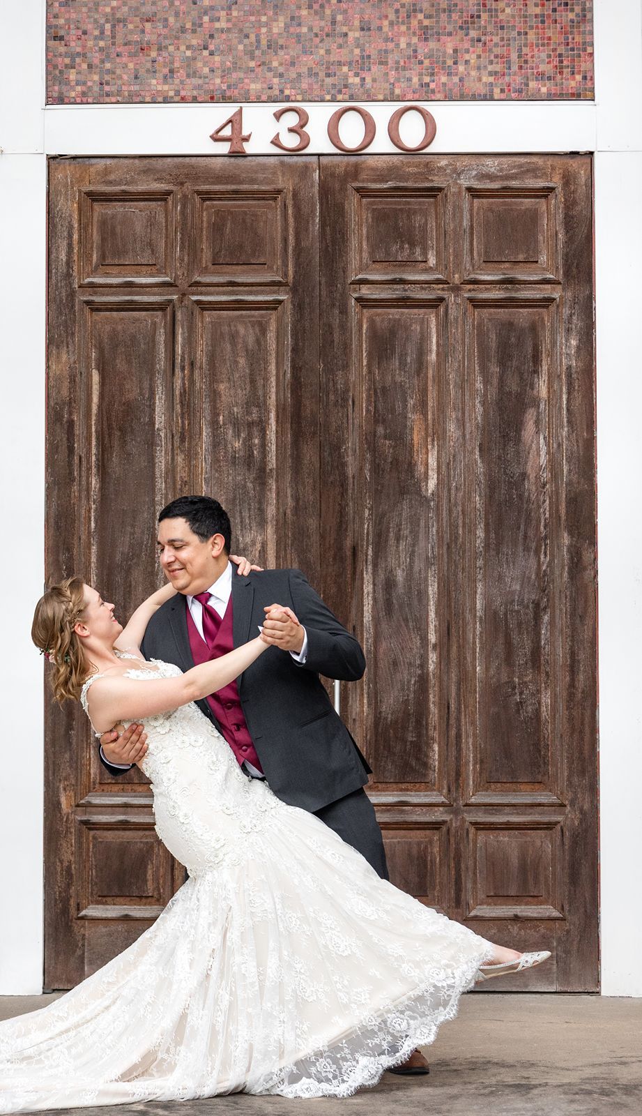 A romantic dance pose in front of rustic wooden doors with the number 4300 above.