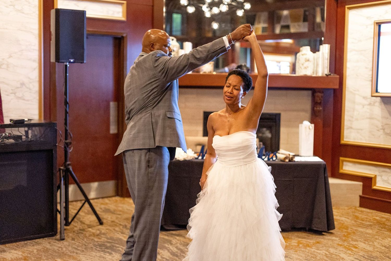 Groom twirls bride in a white ruffled gown during their first dance at a wedding reception.
