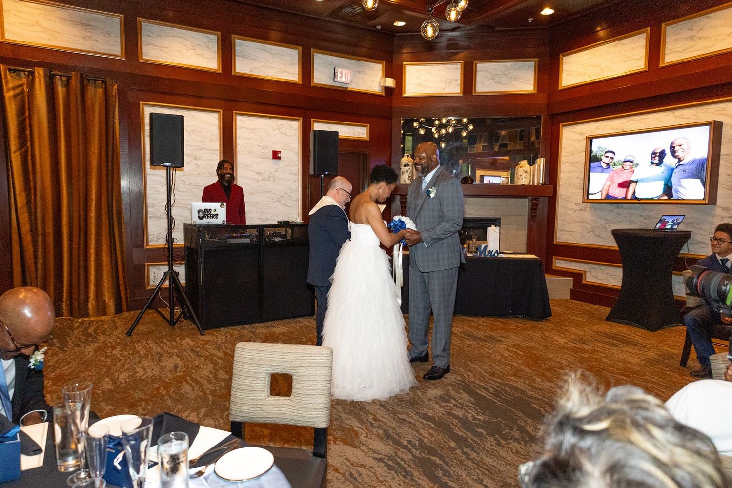 Elegant wedding reception with bride and groom sharing a dance in a warmly lit venue with guests seated nearby.