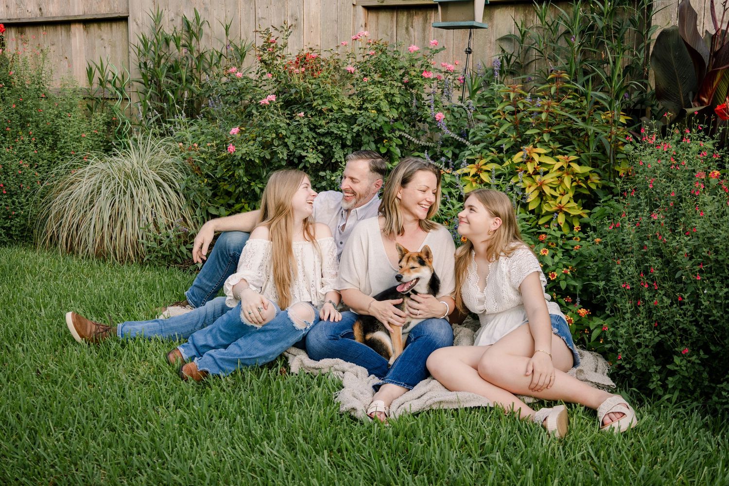 A group sits together on green grass surrounded by a colorful garden with yellow flowers and ornamental grasses.