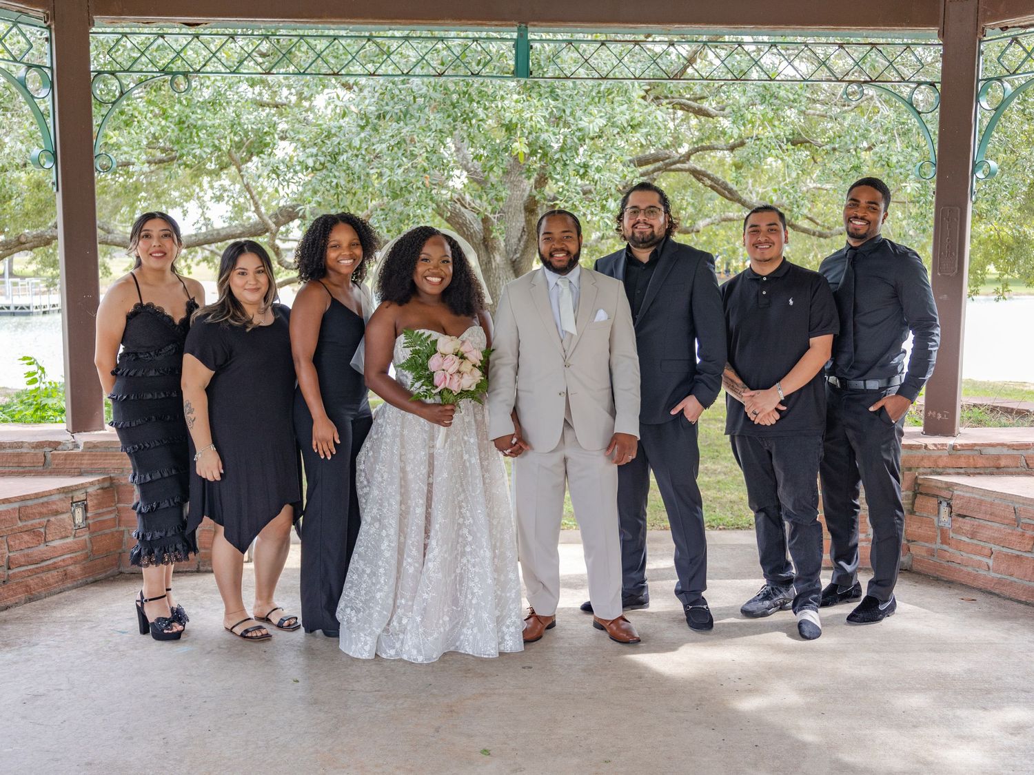 A wedding party poses for a group portrait in matching black and white attire under a covered outdoor area.