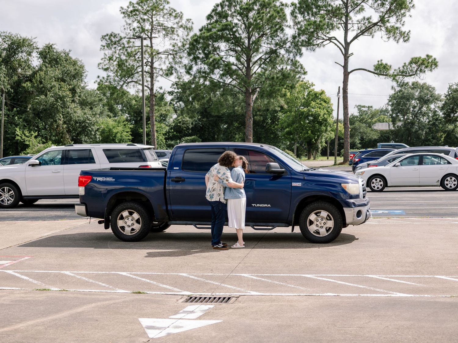 A couple shares an intimate moment in a parking lot next to a blue pickup truck.