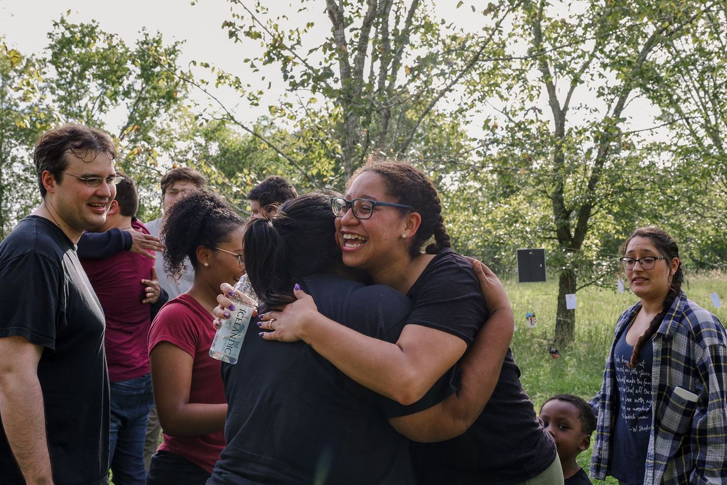 Group of diverse people hugging and smiling outdoors in a green park setting, sharing a joyful moment together.