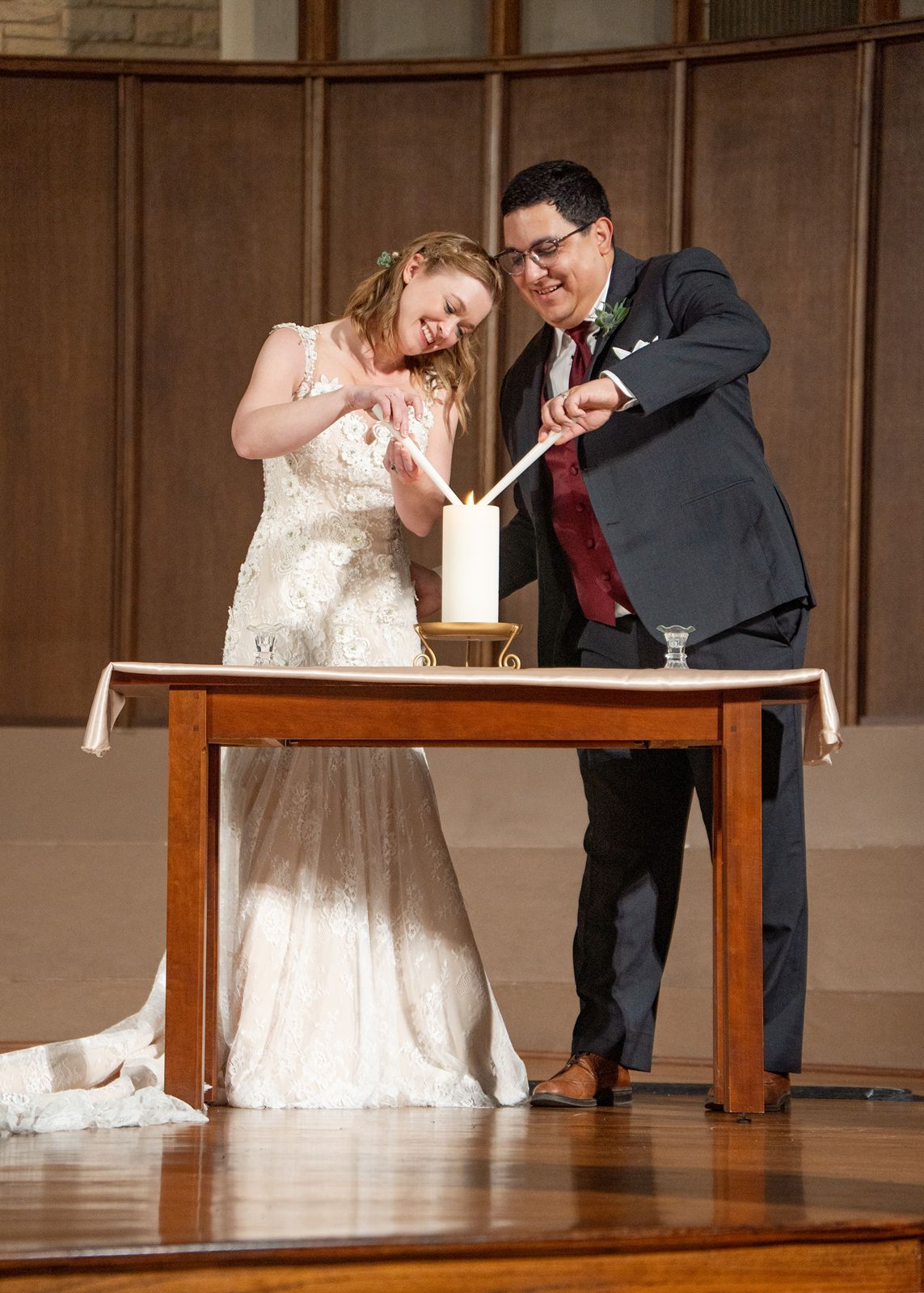 Bride and groom light unity candle together during their wedding ceremony at church altar.