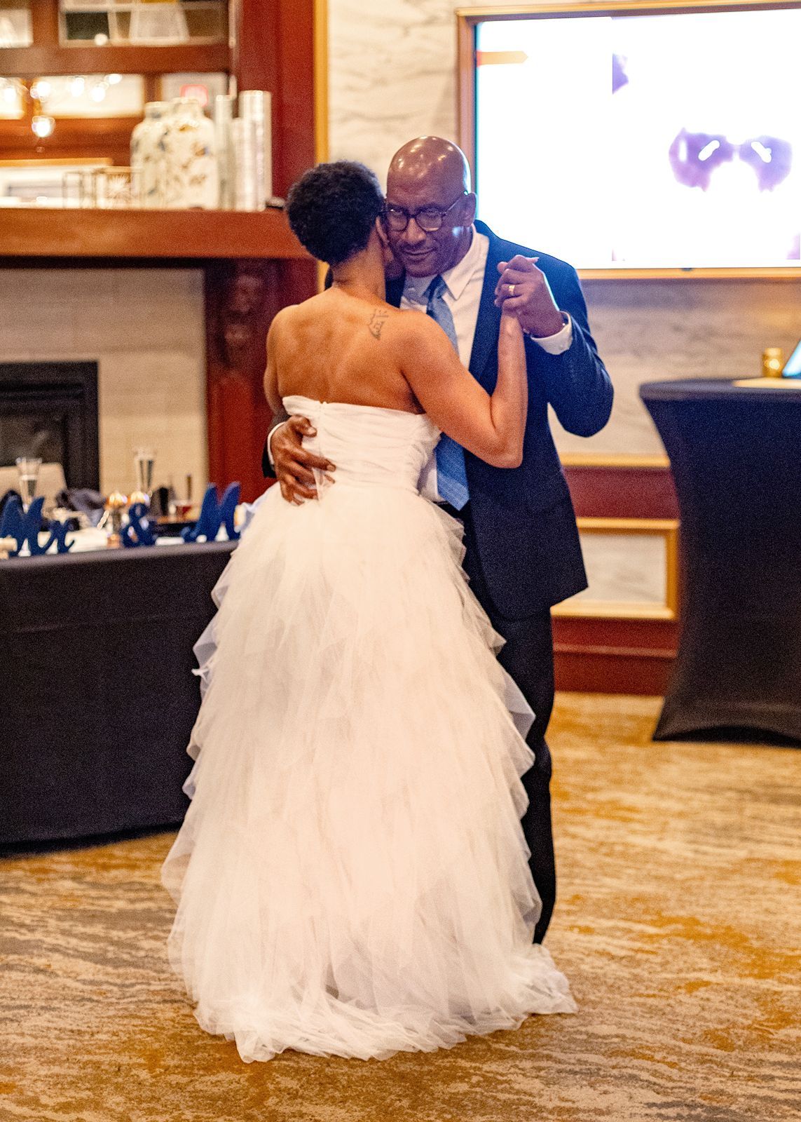 Couple shares romantic first dance at wedding reception, bride in ruffled white gown.