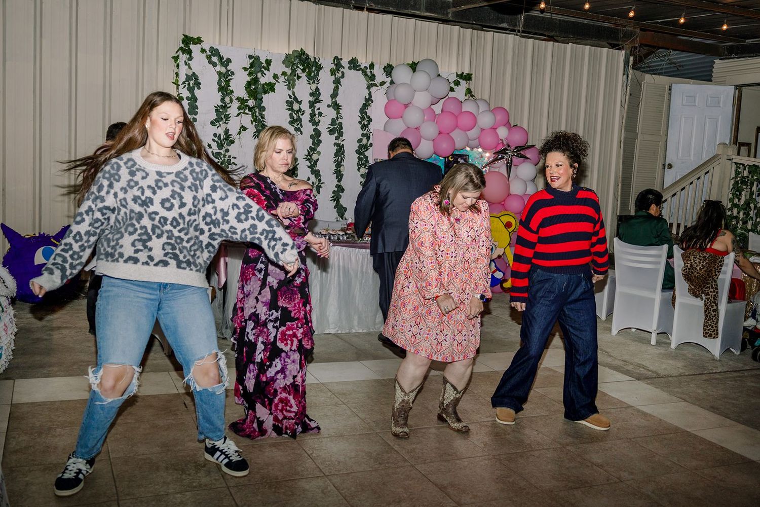 Group of children and adults dancing joyfully at a festive indoor party with balloon decorations.