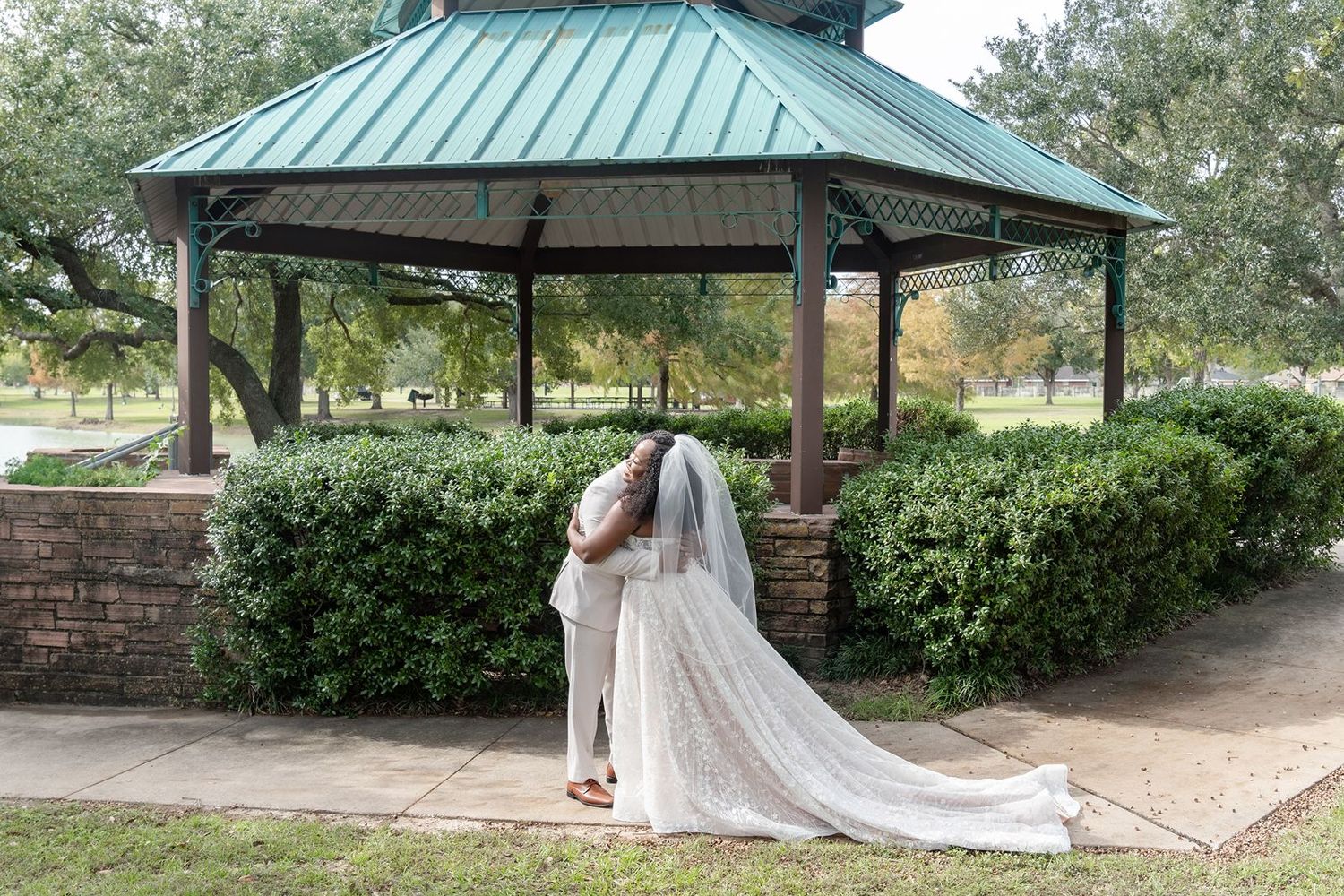 A romantic moment under a green-roofed gazebo surrounded by manicured hedges and brick pathways.