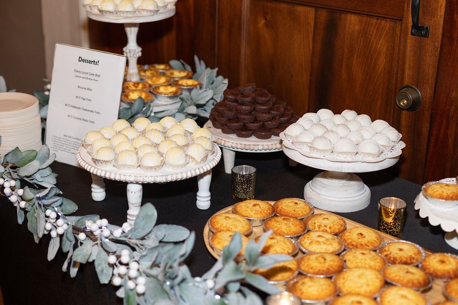 A dessert table display featuring white meringues and golden pastries arranged on tiered platters with eucalyptus decor.