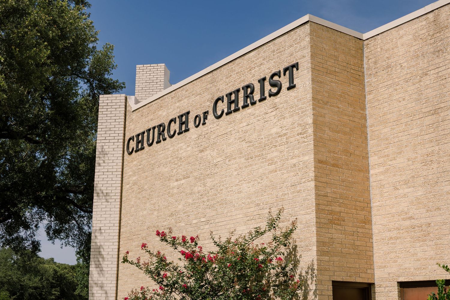 Large brick church building exterior with 'CHURCH OF CHRIST' text mounted on the wall.