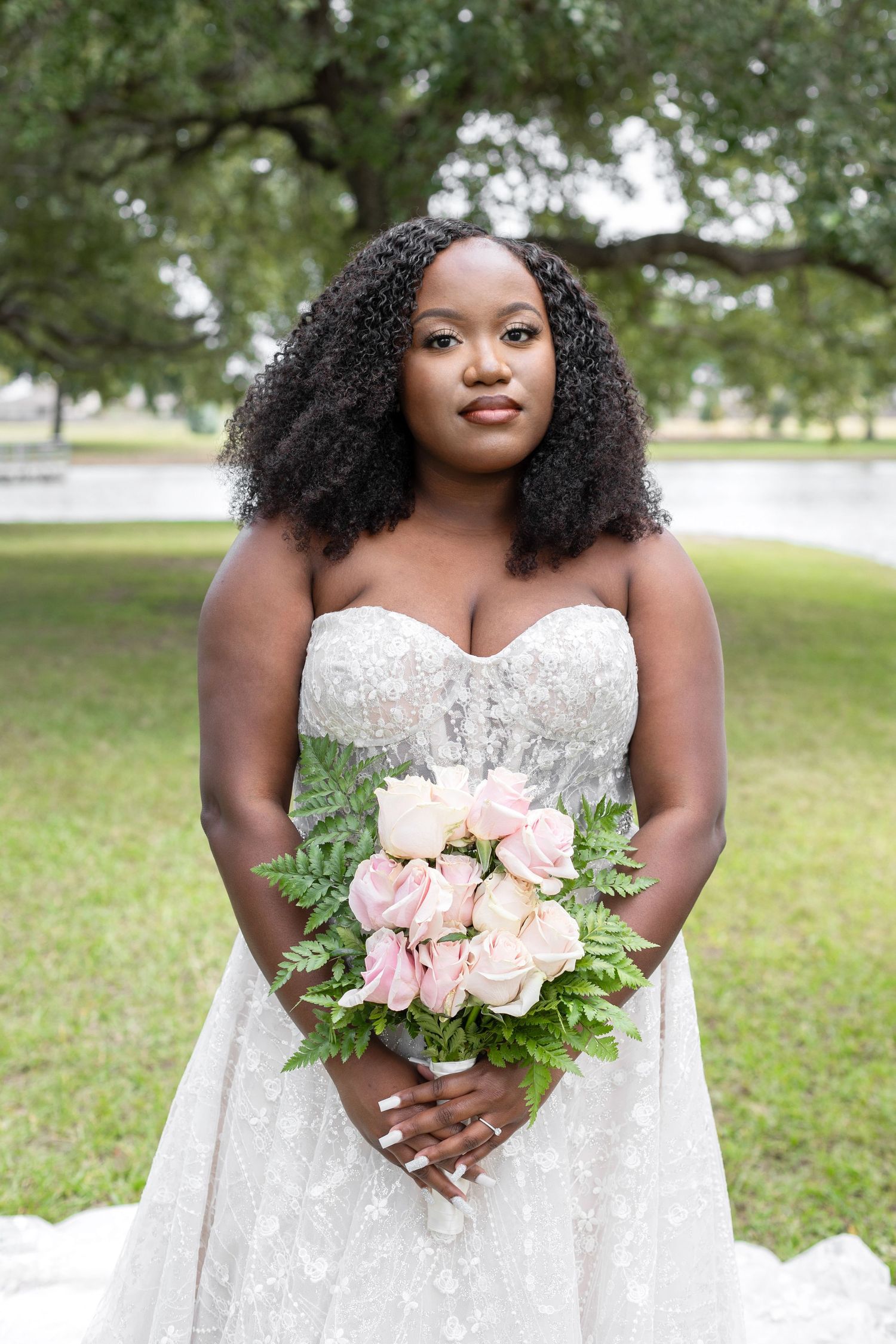 Elegant white lace wedding dress with delicate details holding a soft pink and white floral bouquet.