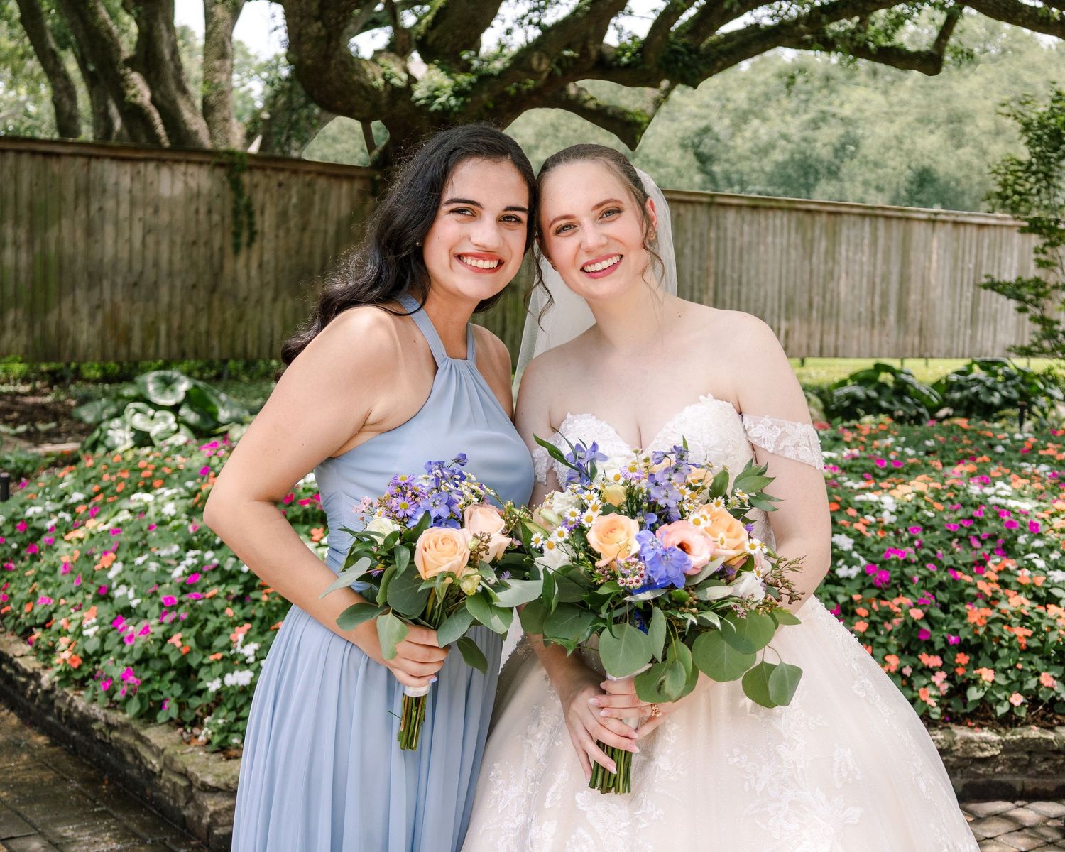 Wedding party members pose with bouquets under shaded garden setting.