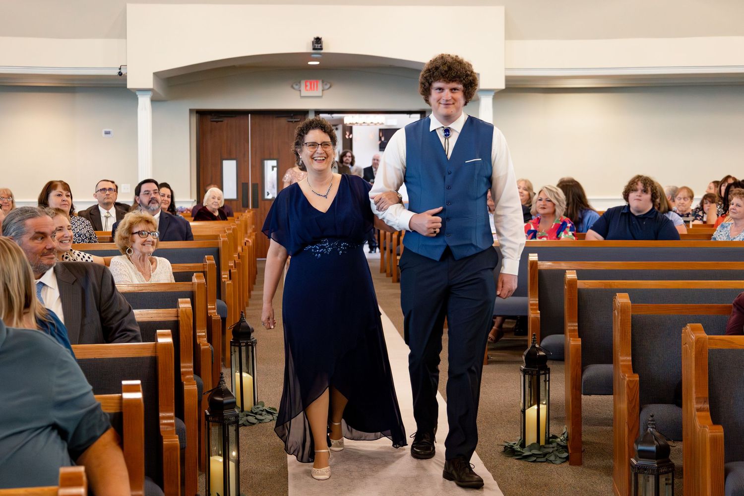 Wedding attendees walk down the center aisle of a bright church sanctuary with modern decor.