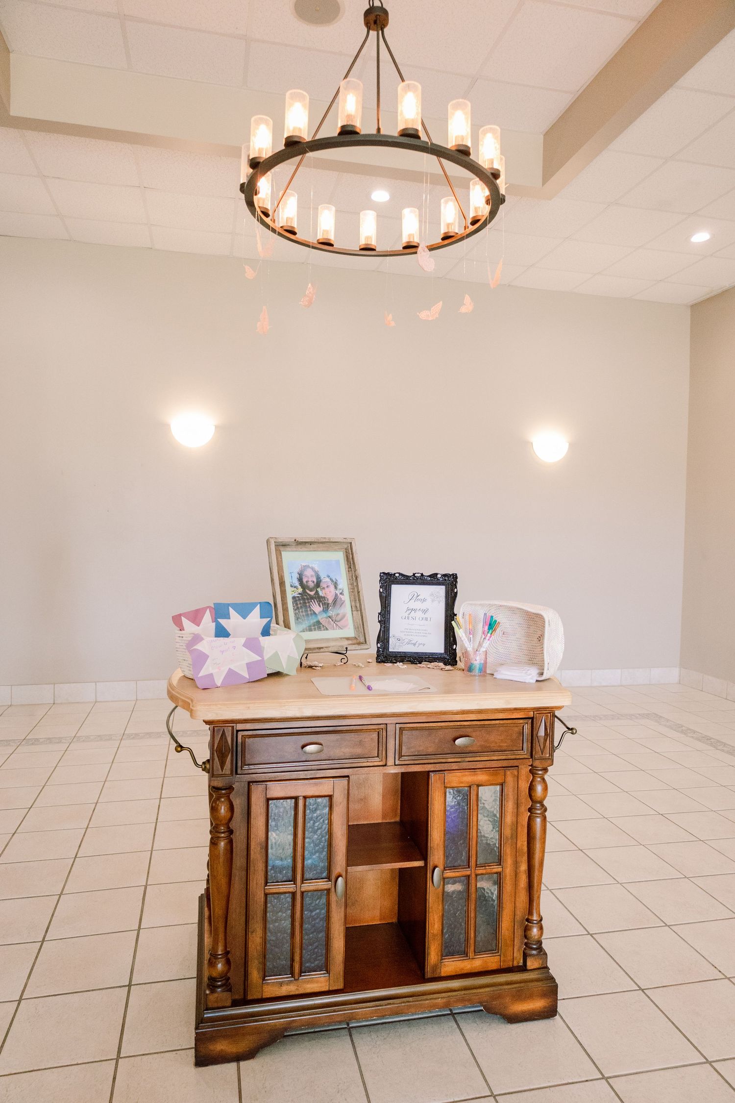 Wooden credenza with glass panels under modern circular chandeliers in a white room.