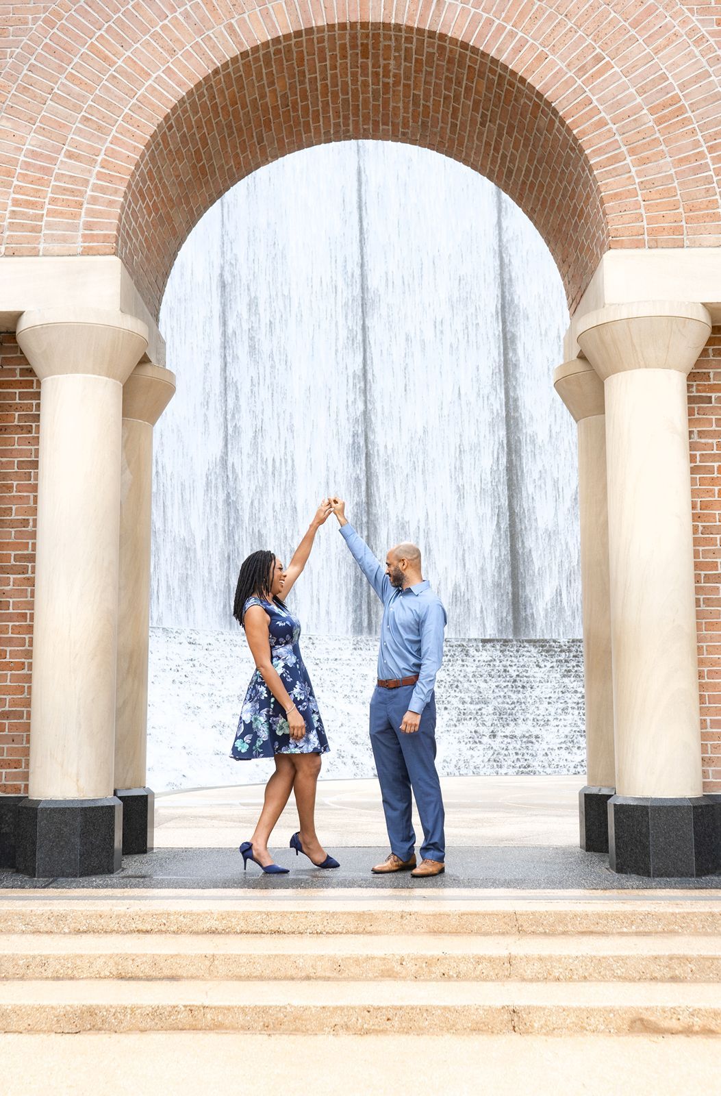 A couple dances and poses together under elegant brick archways in a romantic engagement photo session.