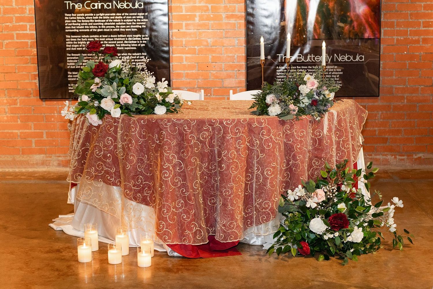 Elegant sweetheart table with floral garland, candles, and lace tablecloth at wedding reception.