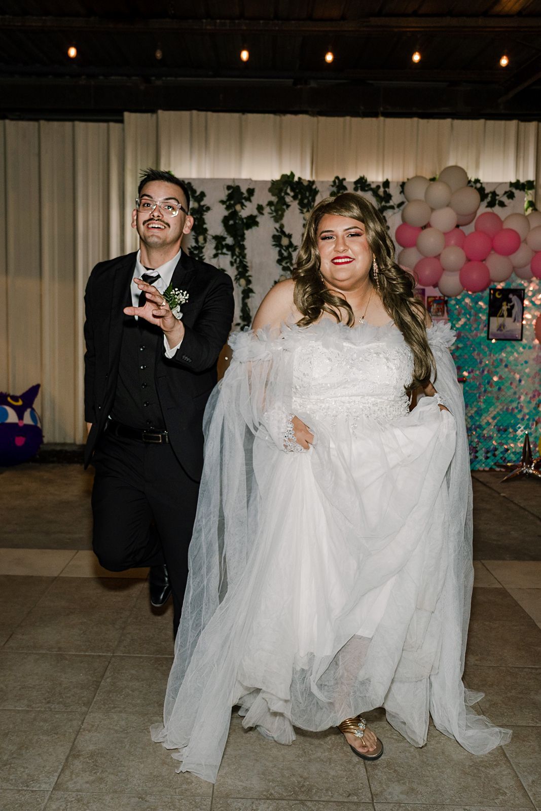 Bride and groom make a grand entrance at their wedding reception with balloons and greenery backdrop.