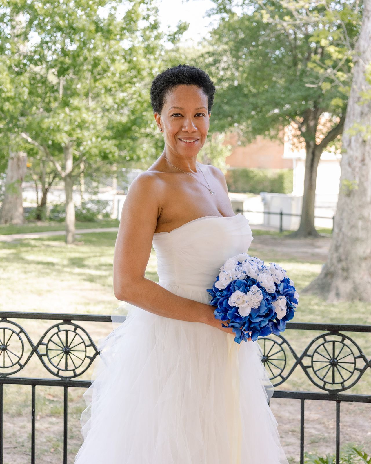 Bride in strapless white tulle gown holding blue hydrangea bouquet outdoors.