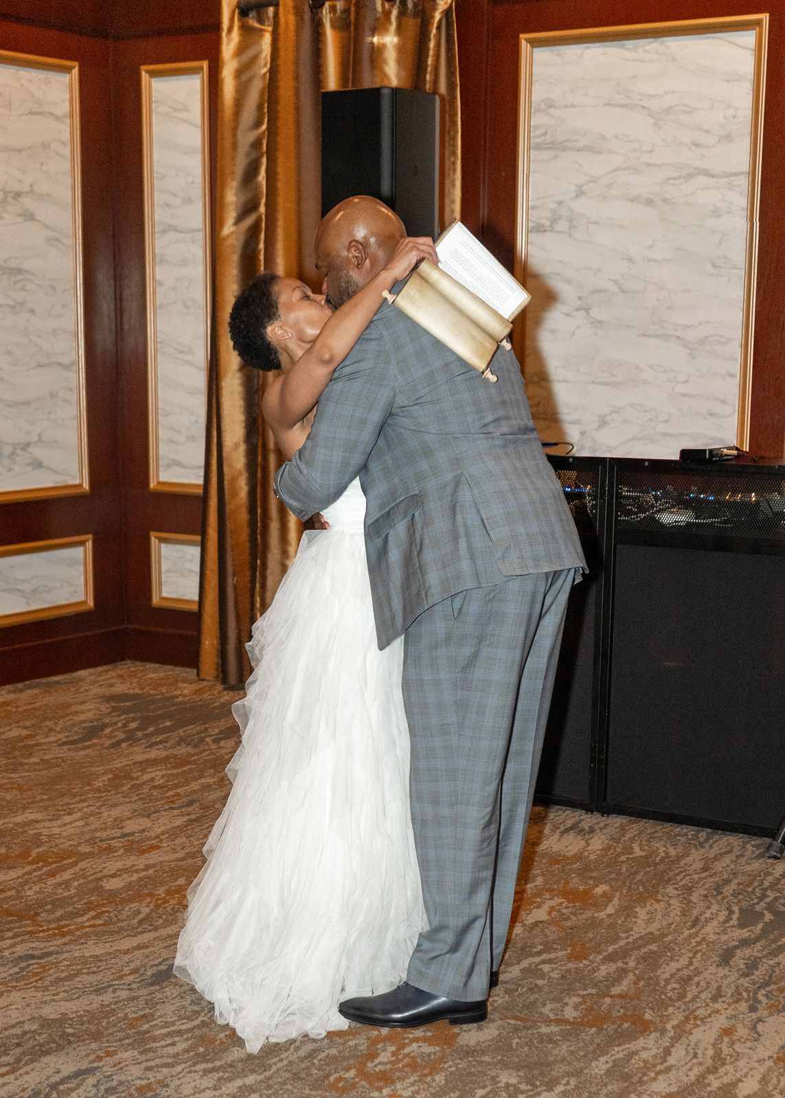 Bride and groom share a warm embrace during their first dance at an elegant wedding reception.