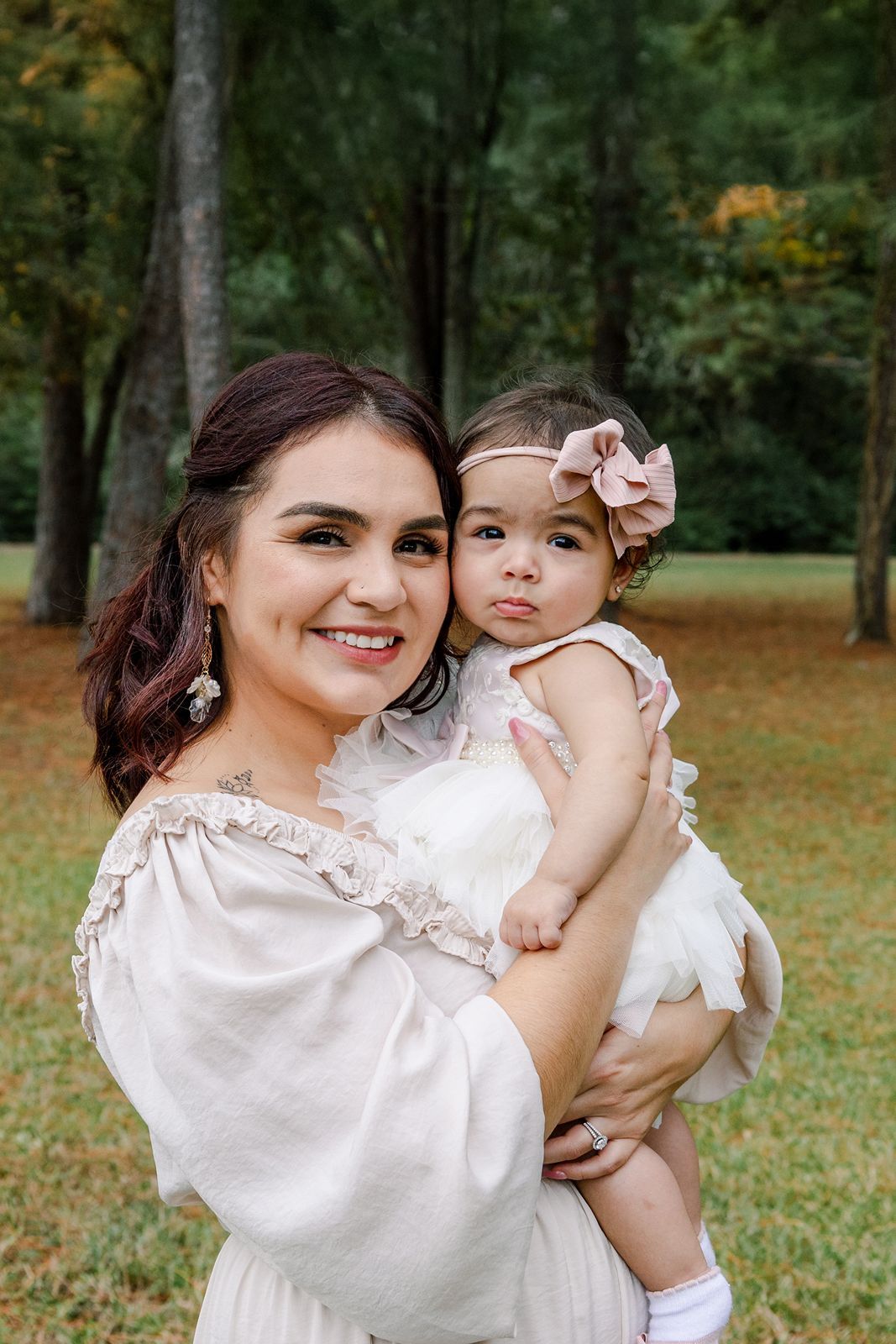 A tender outdoor photoshoot in a park setting showing sweet moments between a parent and child in matching white outfits.