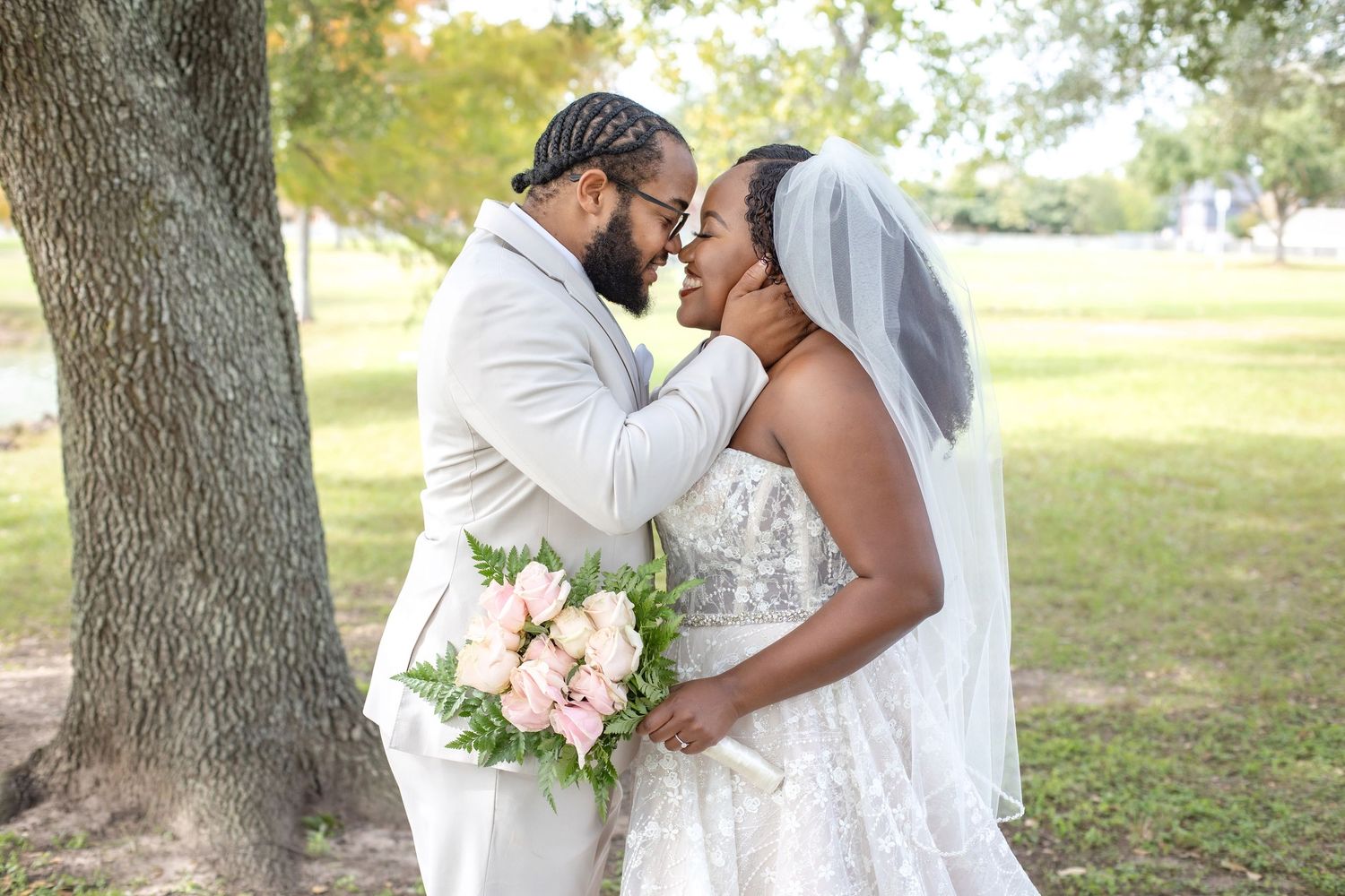 A romantic outdoor wedding portrait with the couple sharing an intimate moment by a tree.