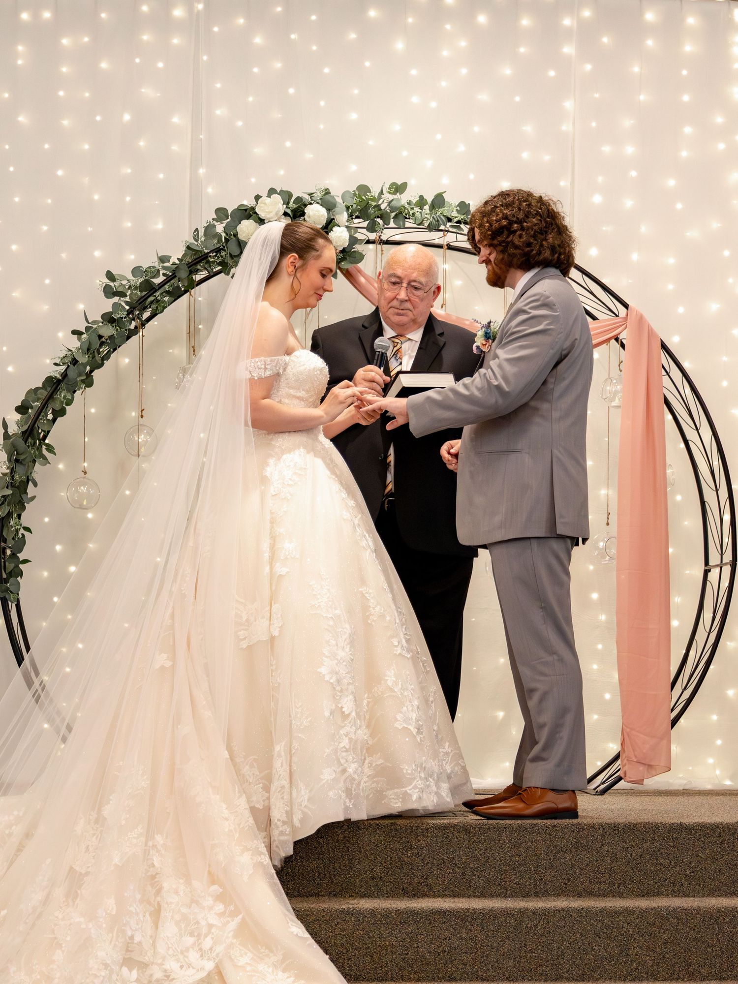 A wedding ceremony under an elegant arch with twinkling lights and floral decorations.