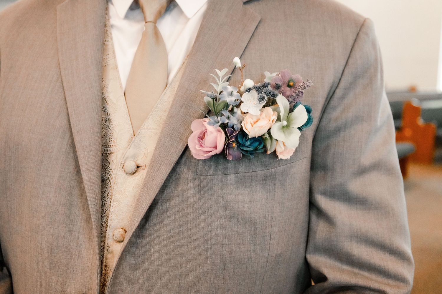 Close-up detail of a pink and white floral boutonniere on a grey suit jacket.