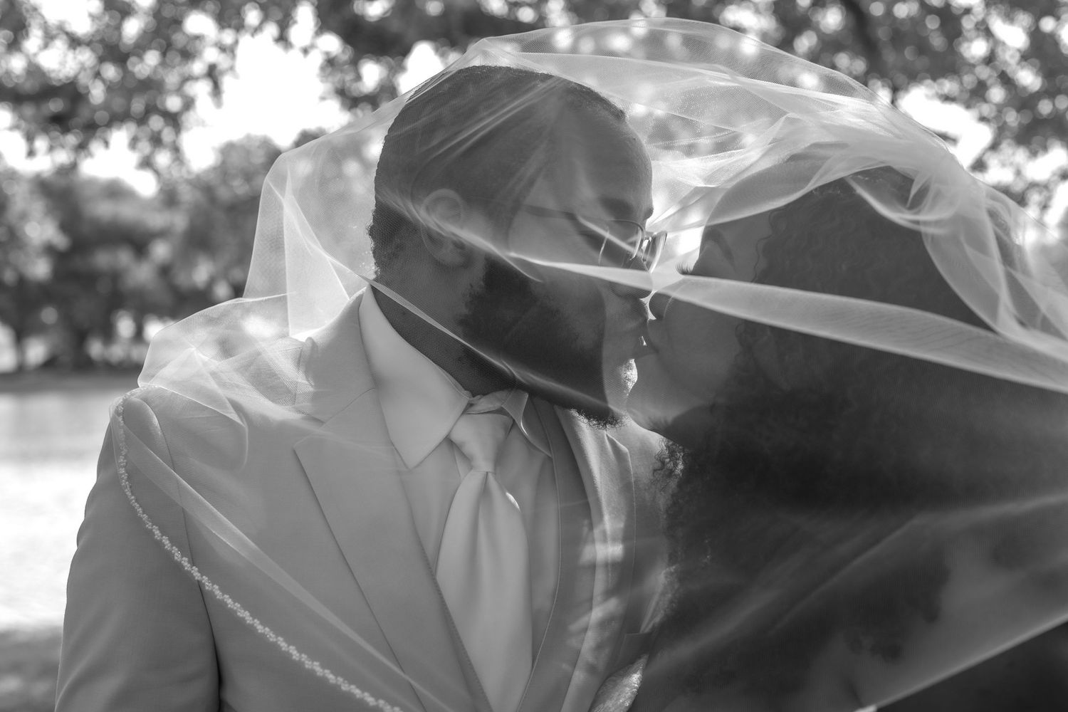 Wedding couple sharing intimate moments under a rustic pavilion with flowing veil.