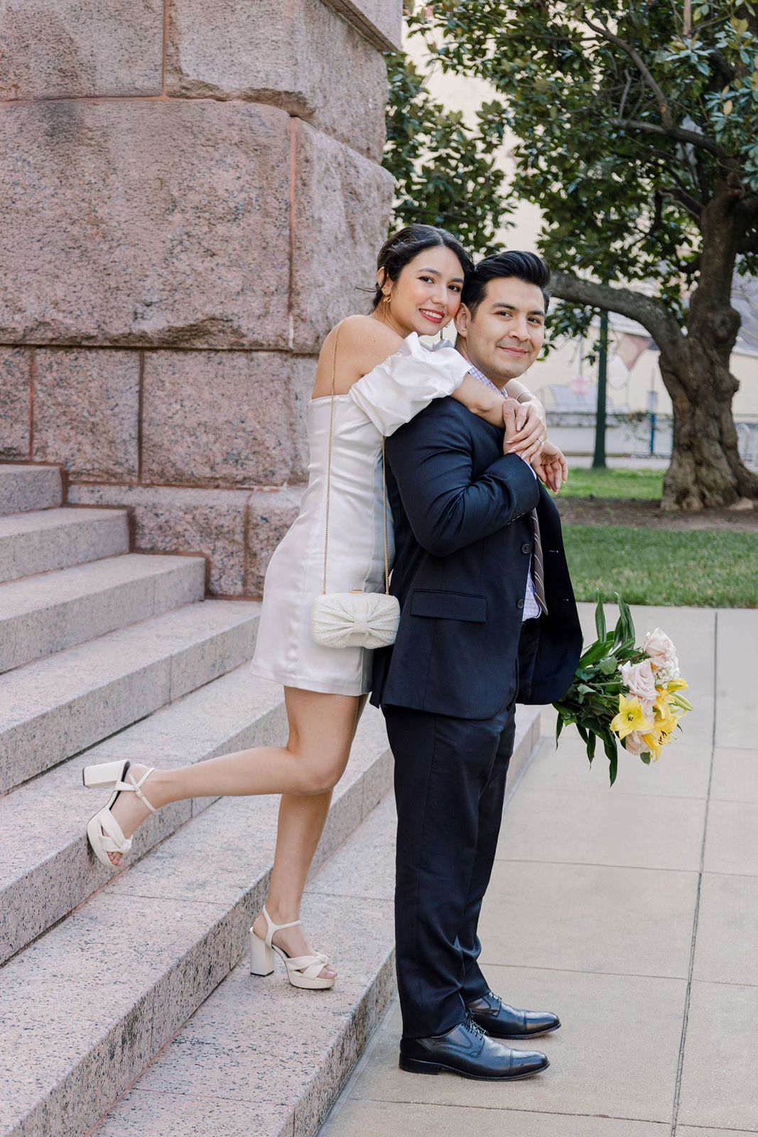 A couple in wedding attire shares playful poses on stone steps during their outdoor photo session.