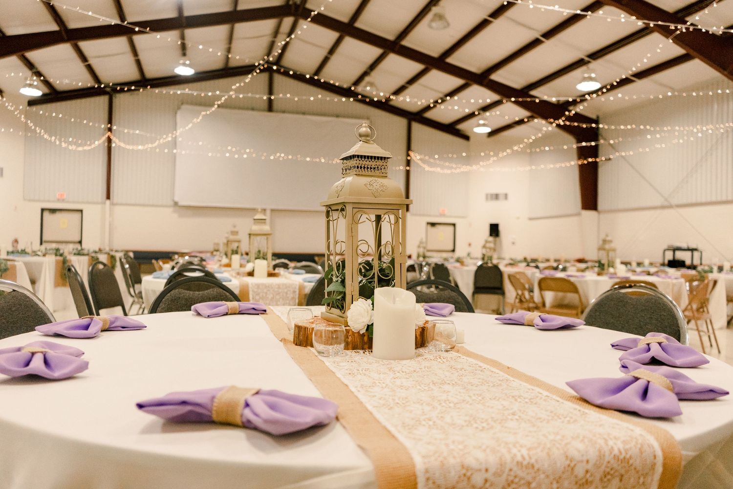 Wedding venue interior decorated with string lights and round tables set up for a reception celebration.