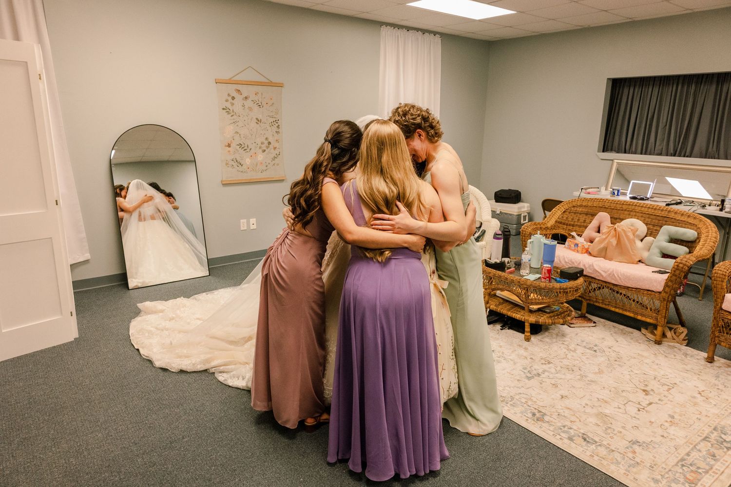 Wedding party members assist with arranging the bride's flowing white dress train in a dressing room.