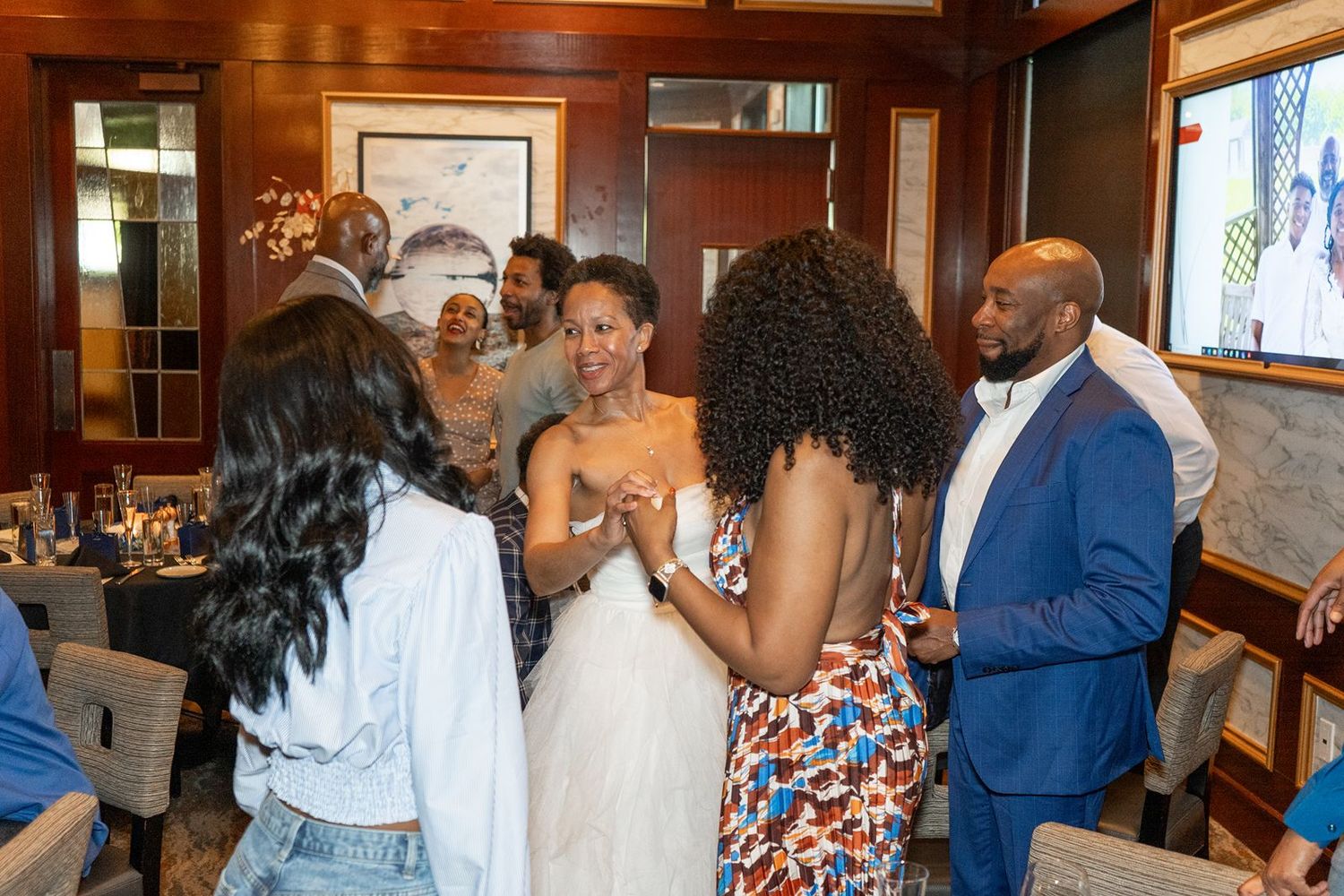 Diverse group of elegantly dressed people socializing and laughing at an upscale indoor gathering or private event.