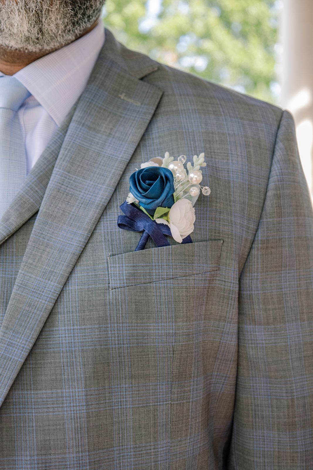 Groom in gray plaid suit with blue rose boutonniere and light blue tie for a wedding.