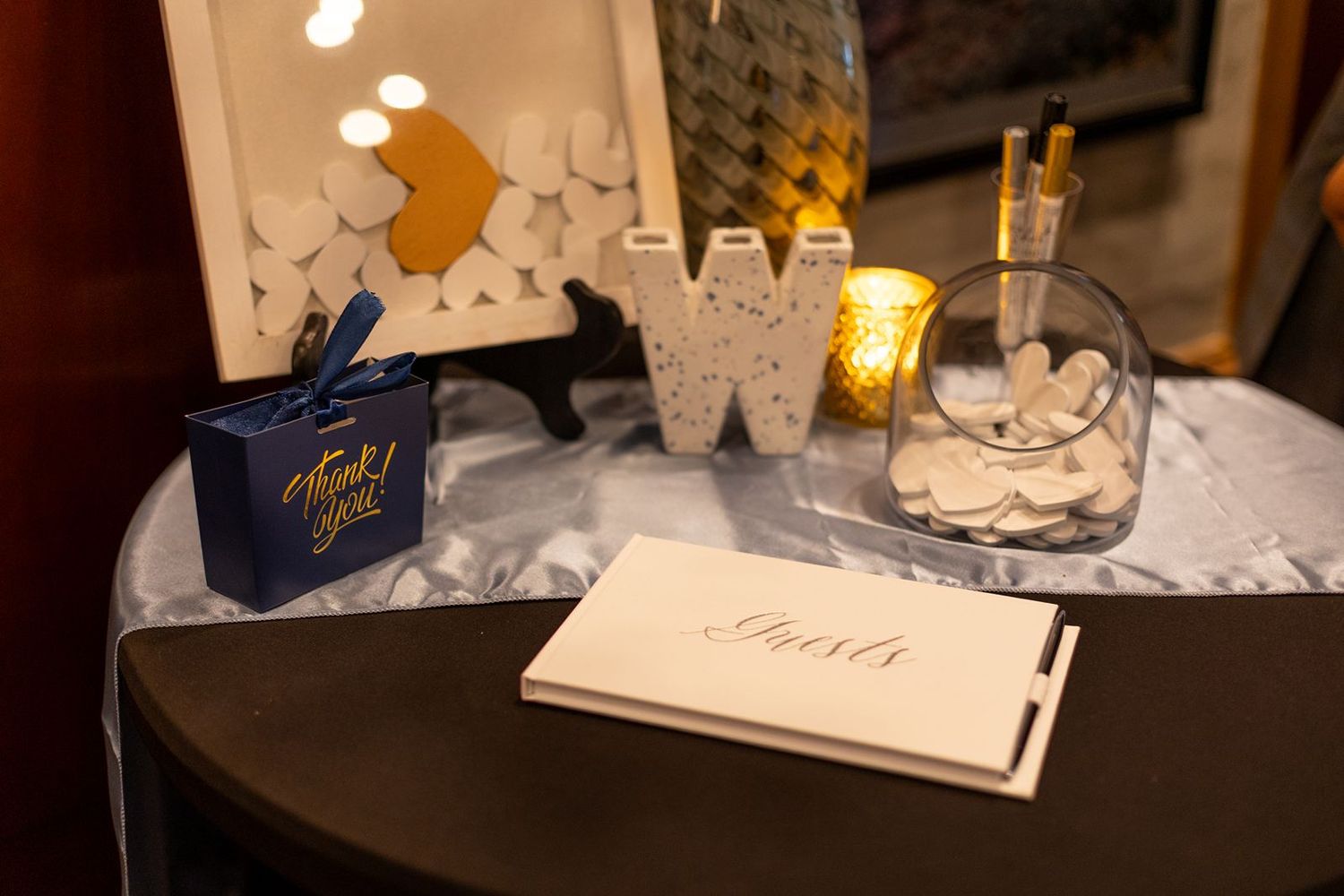 Wedding guest book table with thank you cards, letter W decor, and a glass bowl filled with wooden hearts.