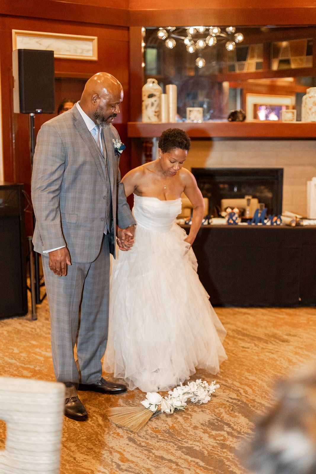 Bride and groom jumping the broom during wedding ceremony at indoor venue.
