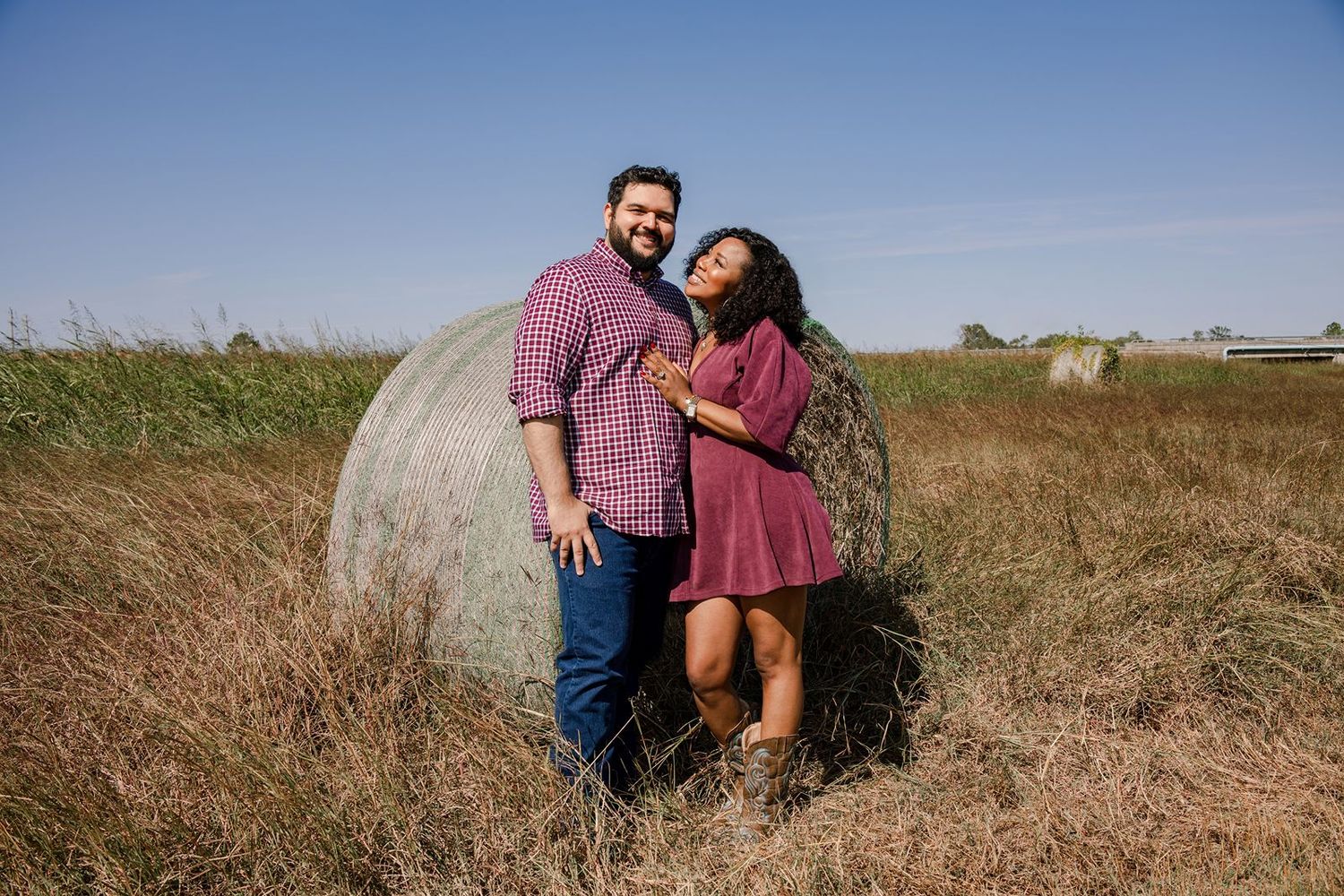 A couple sits together in a golden field during sunset, creating a romantic outdoor portrait.